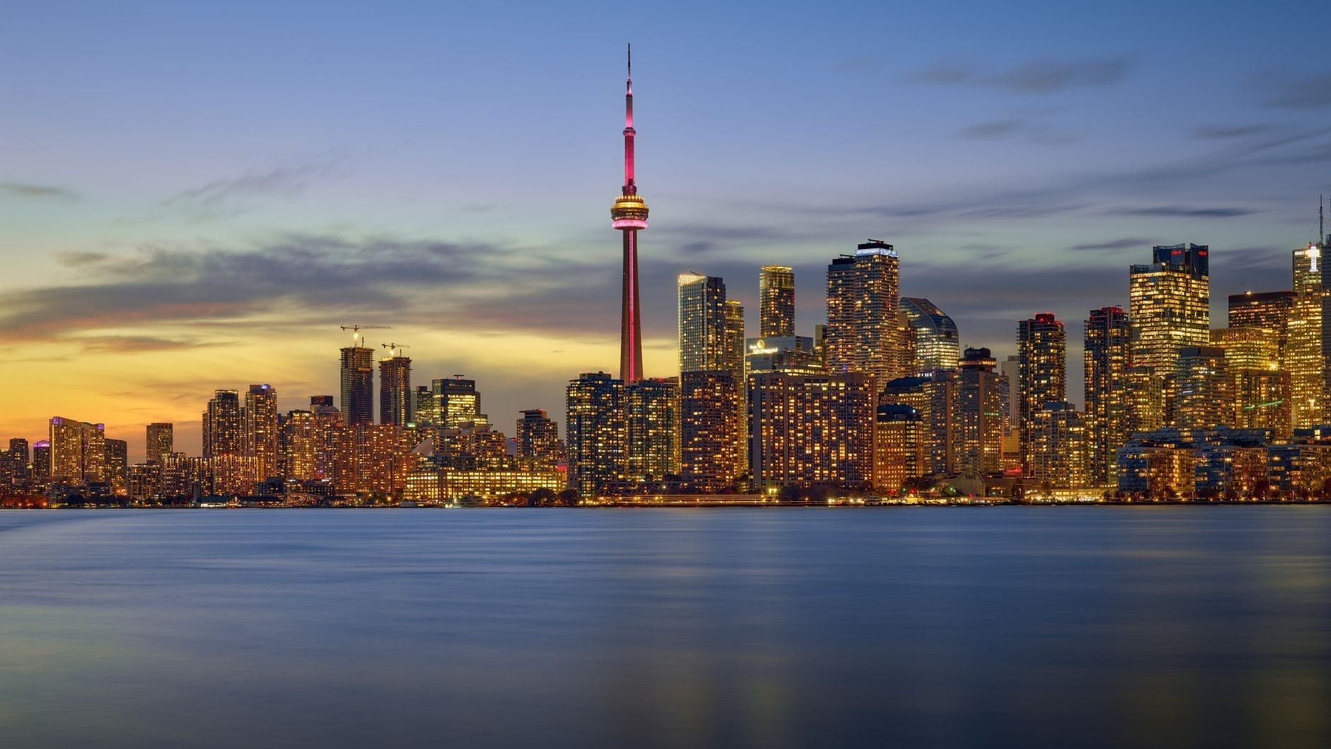 Vista dramática de Toronto ao entardecer, com a CN Tower e as luzes da cidade refletidas no Lago Ontário, transmitindo sofisticação e elegância.