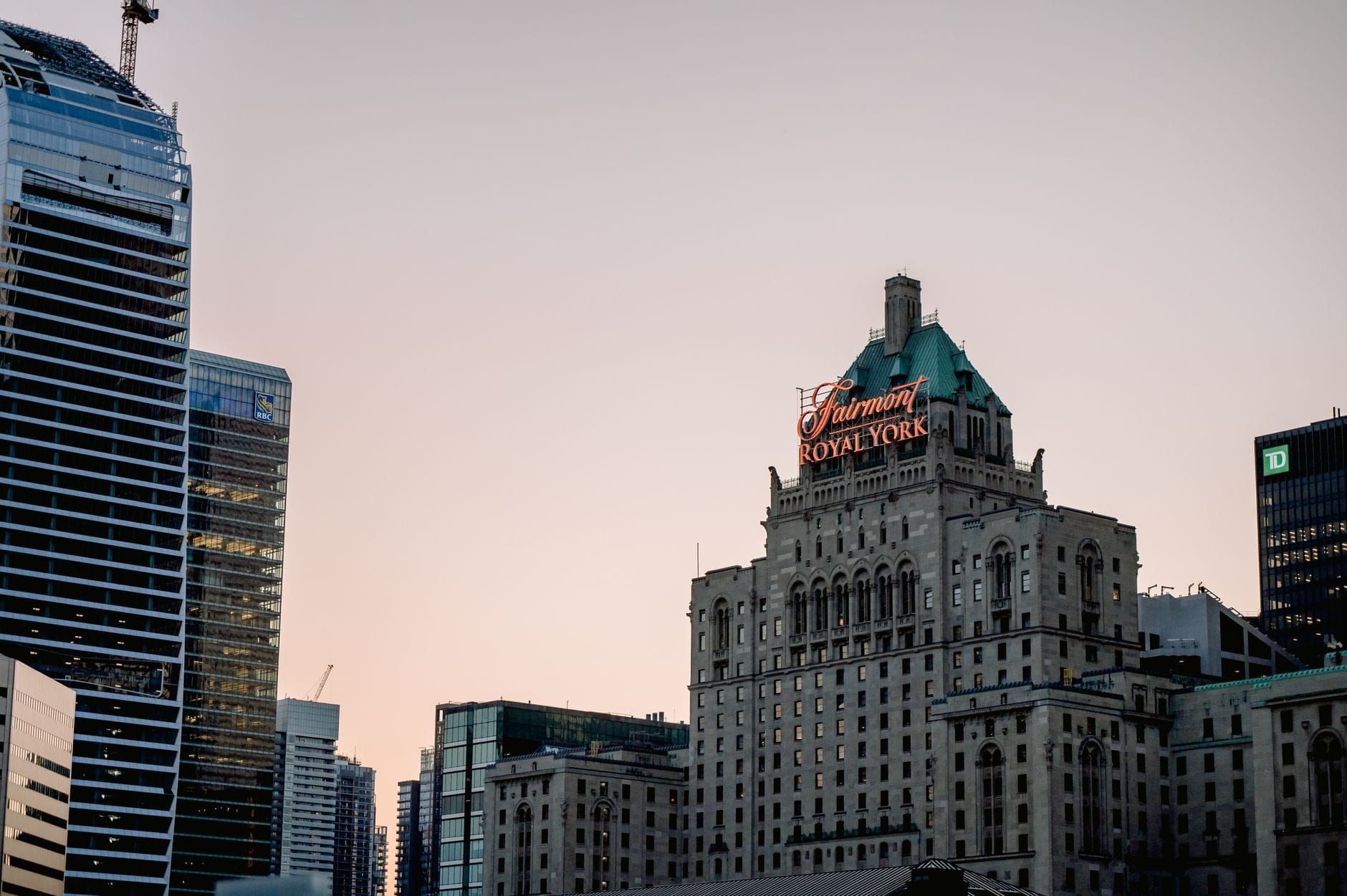 O histórico hotel Fairmont Royal York com sua iluminada placa vermelha em meio aos arranha-céus do centro de Toronto ao entardecer.