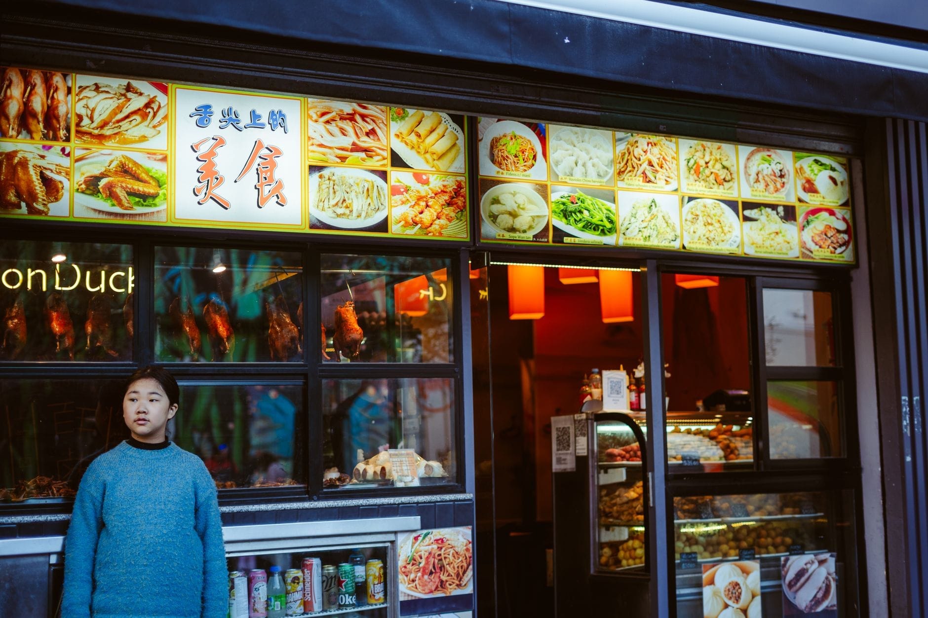 Fachada de restaurante chinês com fotos coloridas de vários pratos na vitrine e uma pessoa em pé do lado de fora.