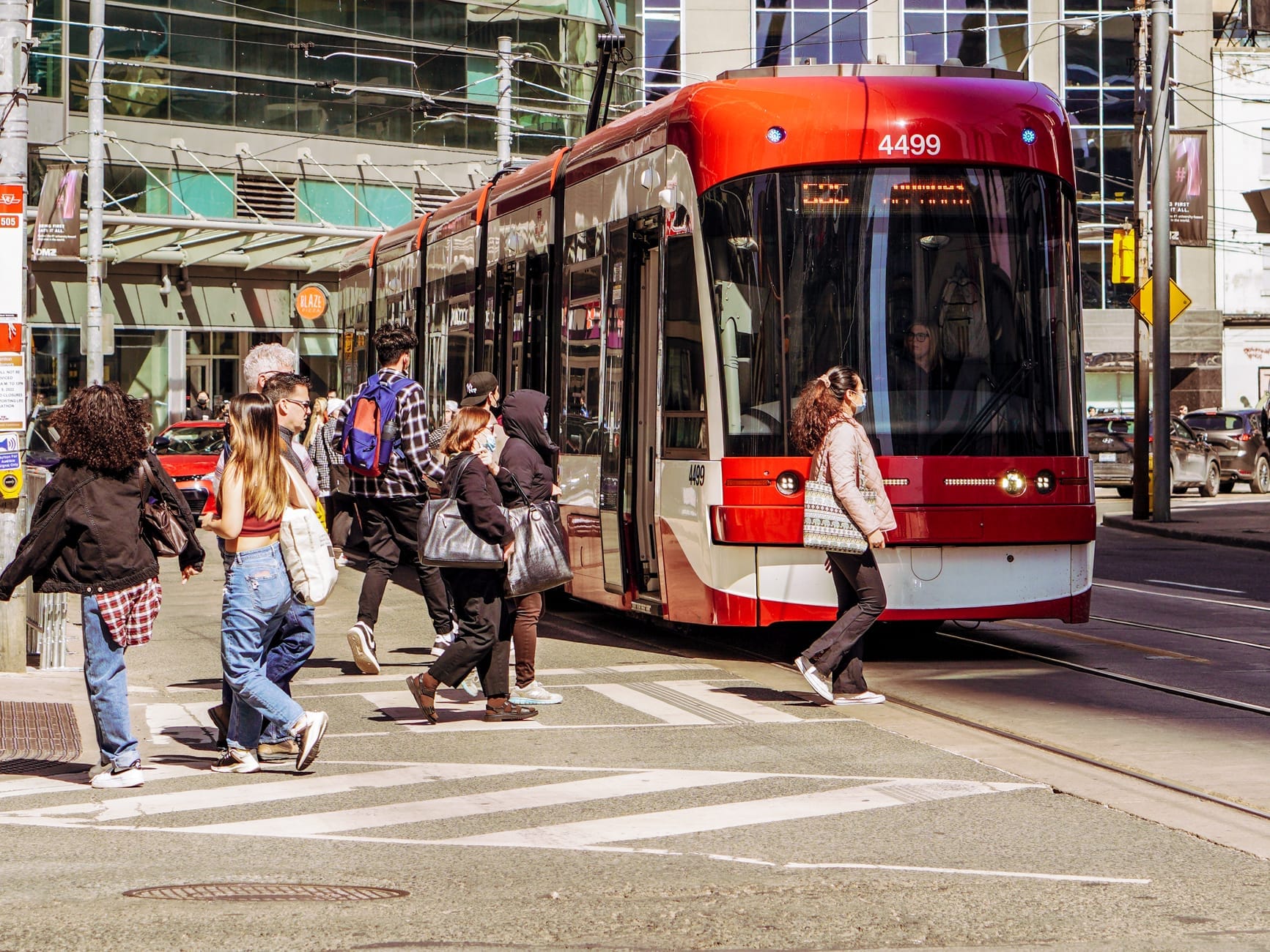Pessoas atravessando a rua em frente a um moderno bonde vermelho e branco de Toronto em um cruzamento urbano durante o dia.