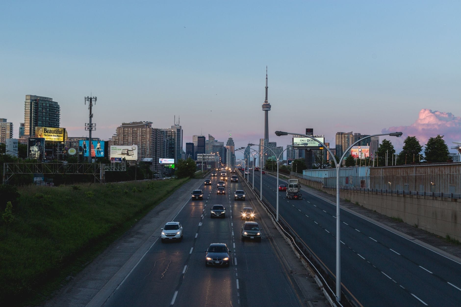 Vista do horizonte de Toronto com a CN Tower e tráfego saindo da cidade pela rodovia ao entardecer.