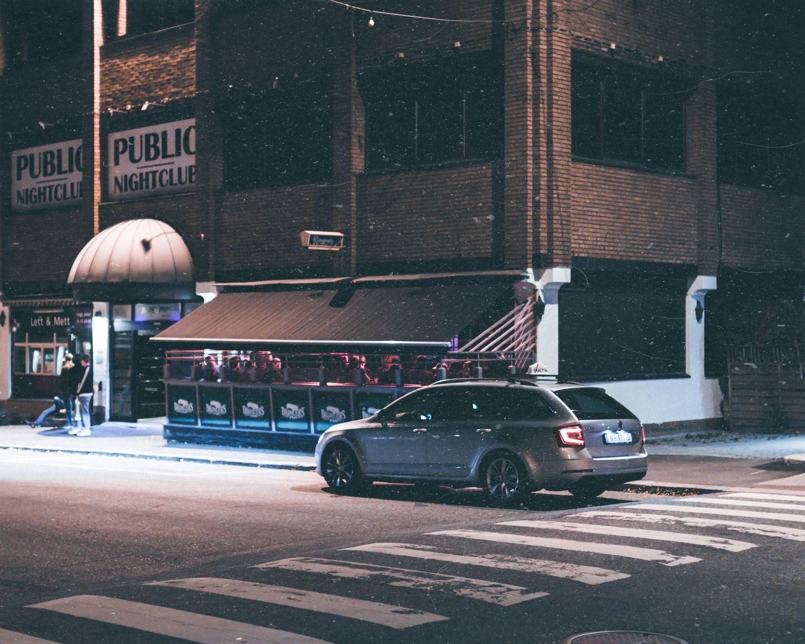Vista noturna do exterior do Public Nightclub em Toronto com um carro escuro estacionado na frente e as luzes da cidade iluminando a cena.