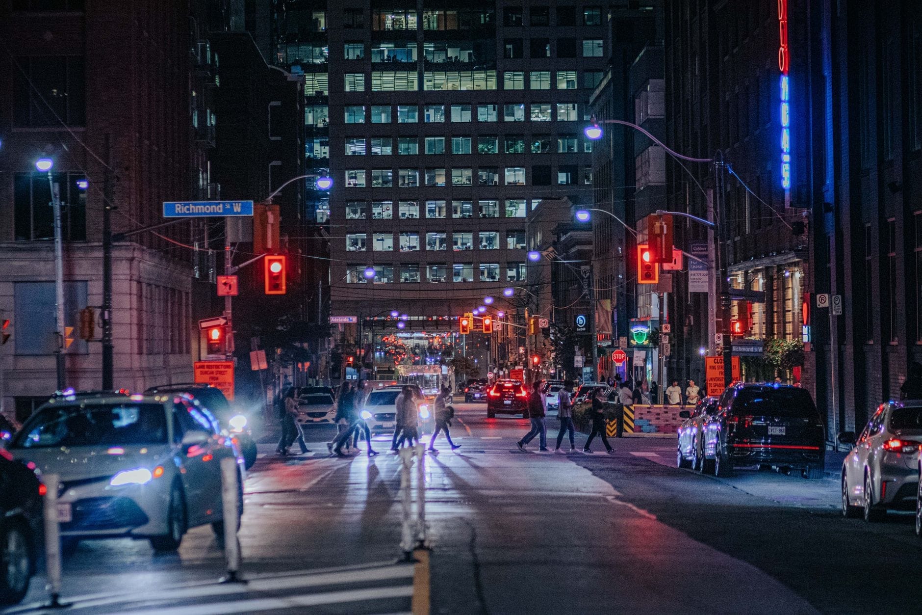 Vista noturna de uma movimentada rua do centro de Toronto perto de Richmond Street, pedestres atravessando, carros, luzes da cidade e edifícios.