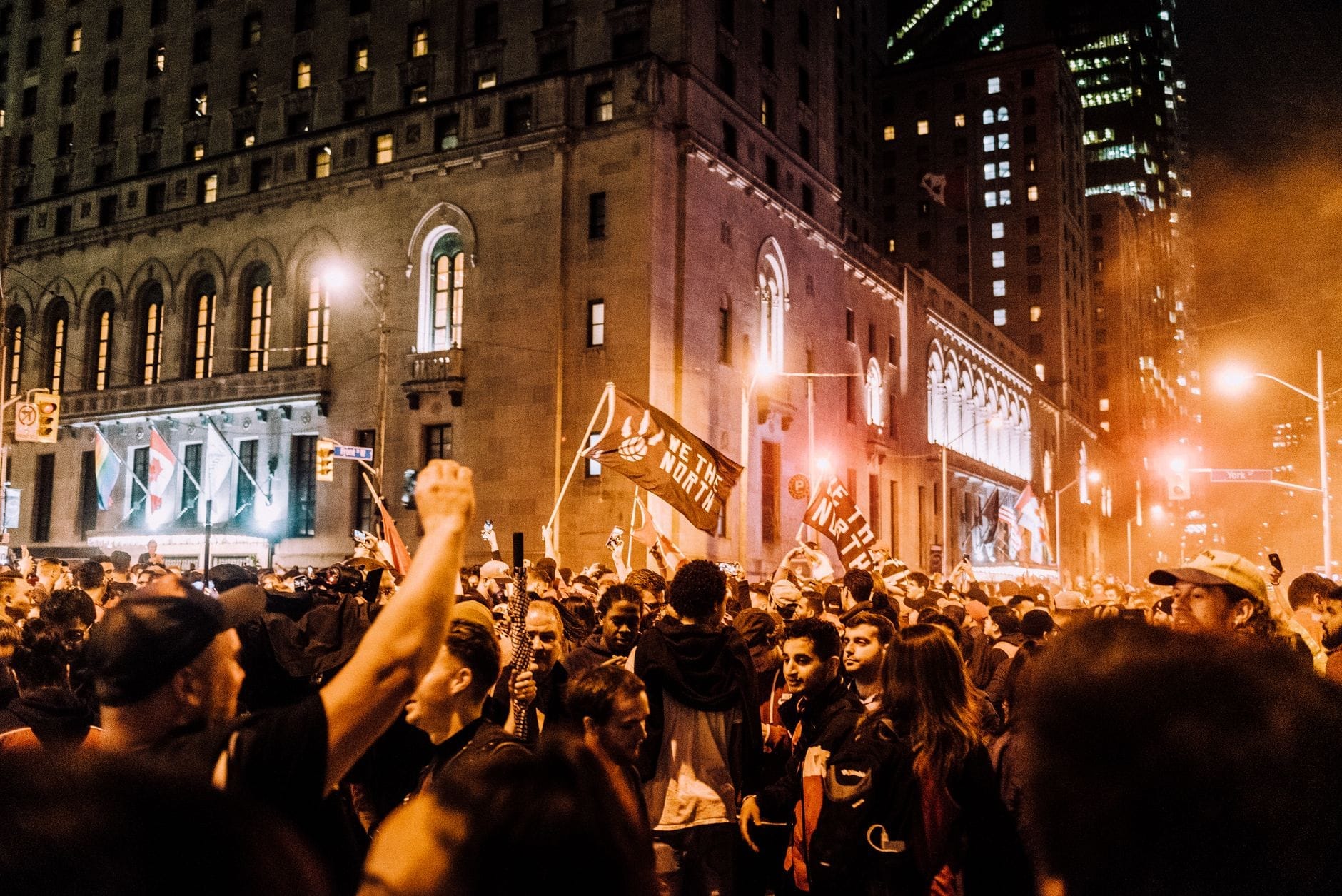 Grande foule dense de personnes remplissant une rue de Toronto la nuit avec des bâtiments et des lumières de la ville en arrière-plan.