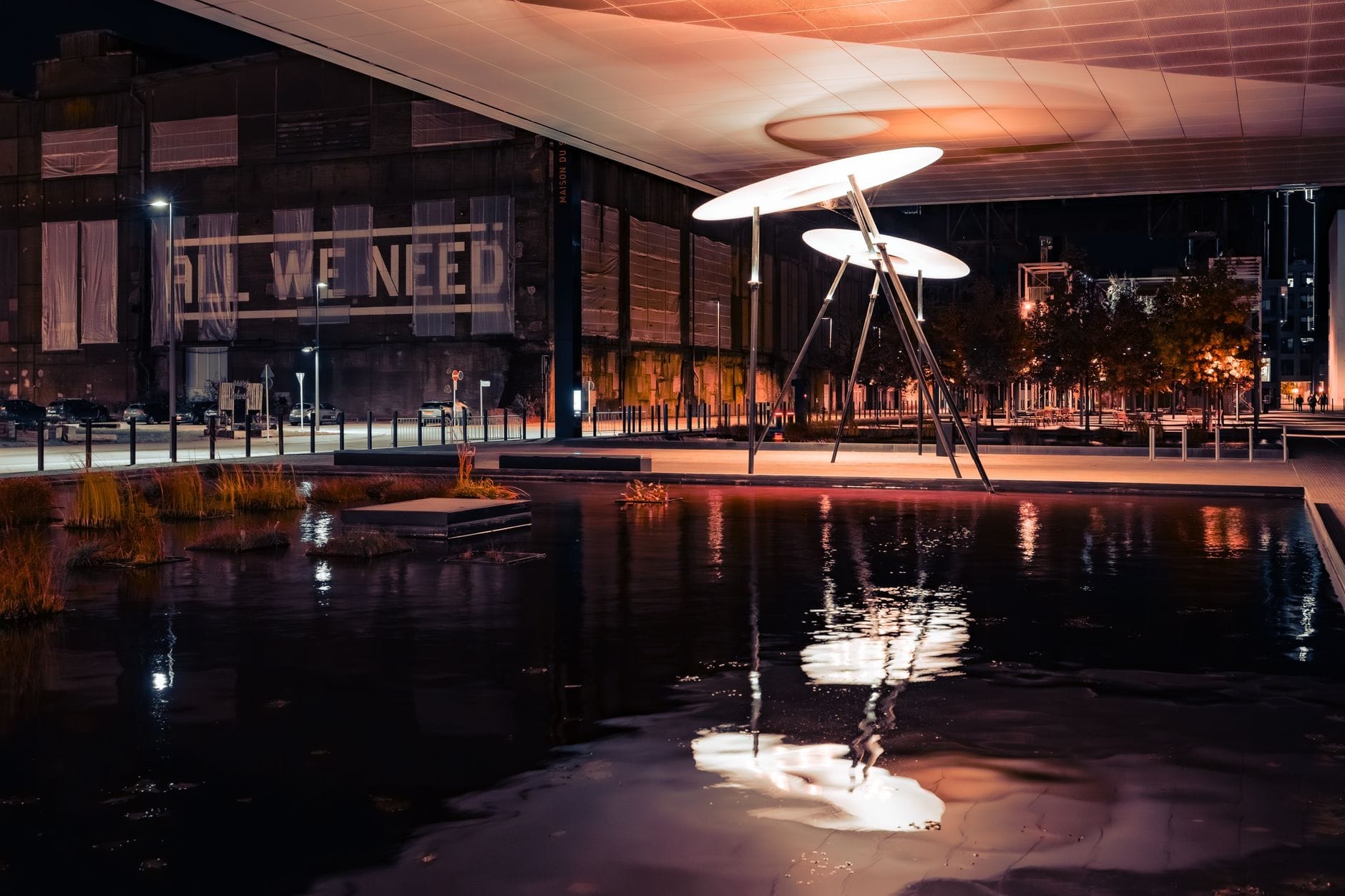 Installation artistique nocturne en plein air avec de grandes structures circulaires illuminées au-dessus de l'eau, cadre urbain moderne et bâtiments au loin à Toronto.