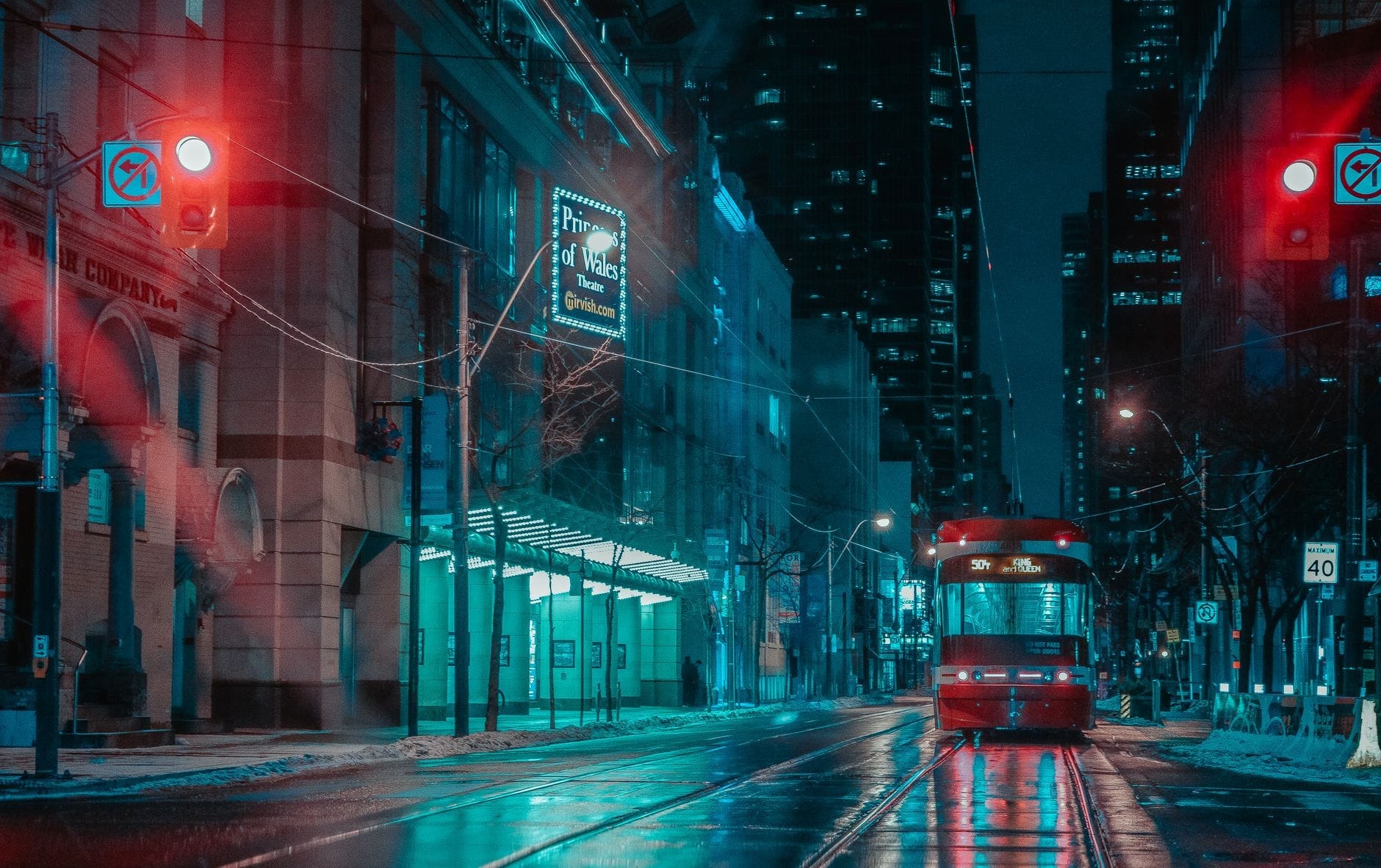 Un tramway de Toronto circule dans une rue mouillée illuminée par des néons la nuit, entouré de grands immeubles et de feux de circulation brillants.