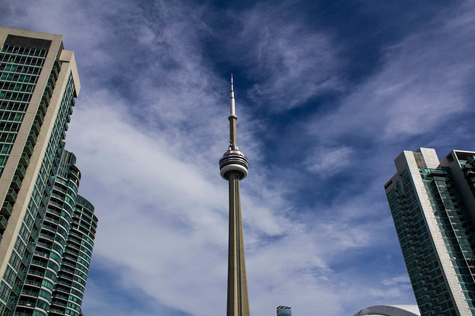Skyline de Toronto com a CN Tower e modernos arranha-céus sob um céu parcialmente nublado.