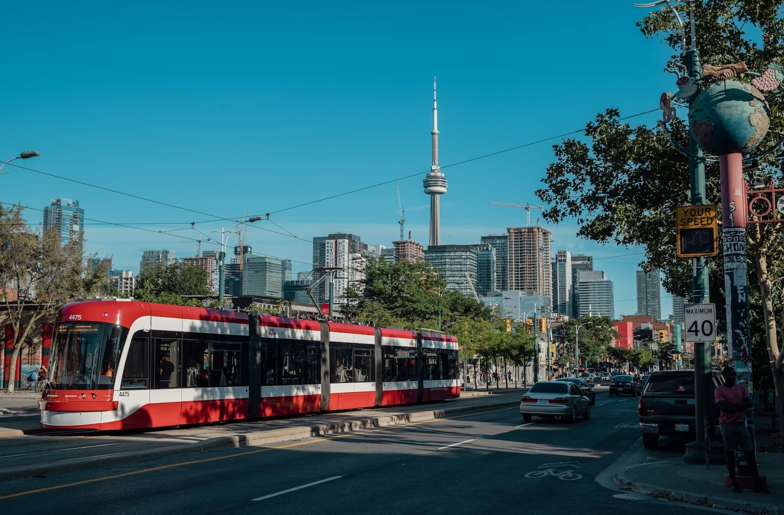 Bonde de Toronto percorrendo o centro da cidade com a CN Tower e o horizonte urbano ao fundo em um dia ensolarado.