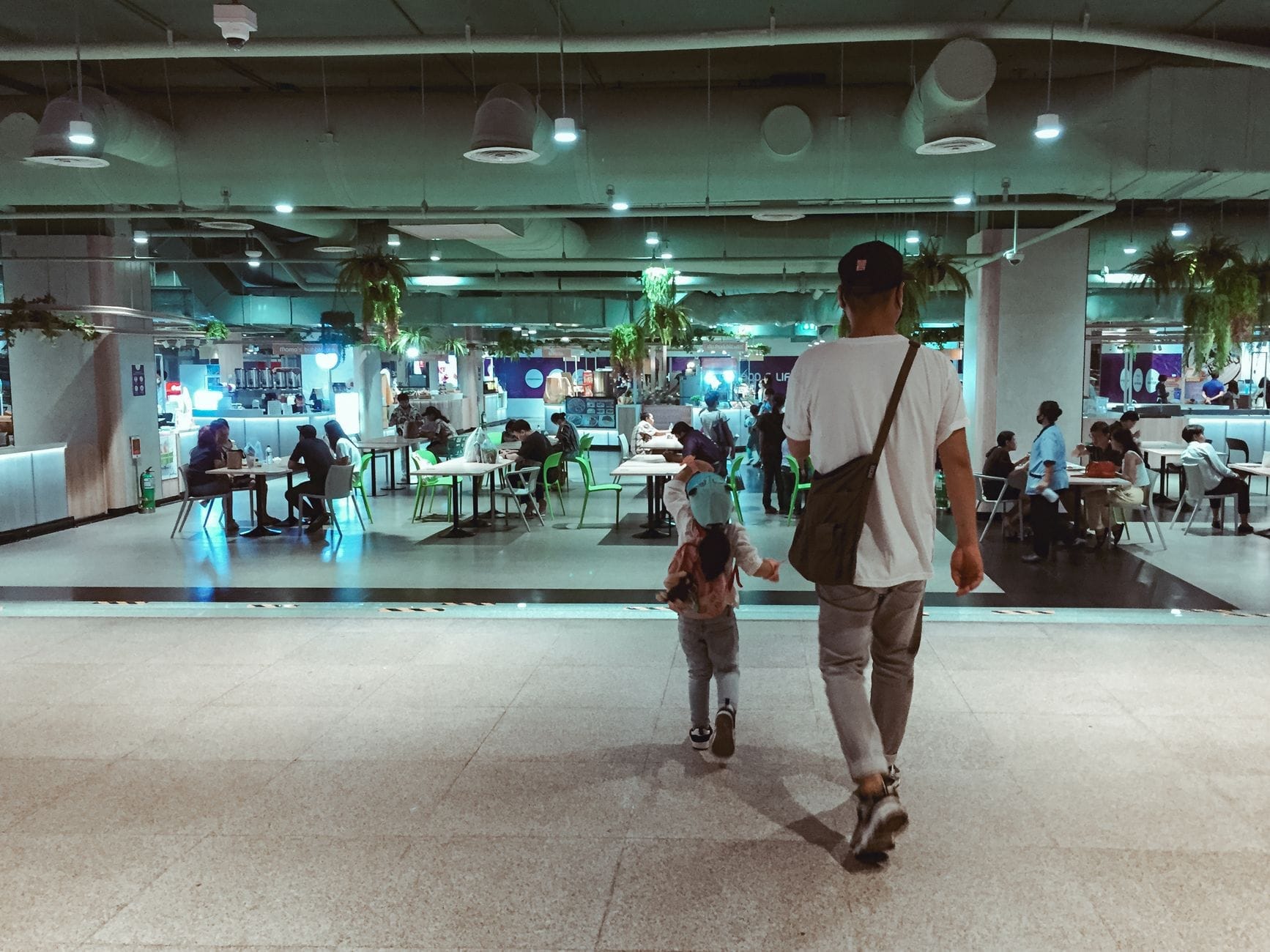 Pessoas sentadas e jantando em mesas em uma praça de alimentação subterrânea moderna e bem iluminada com várias lanchonetes ao fundo.