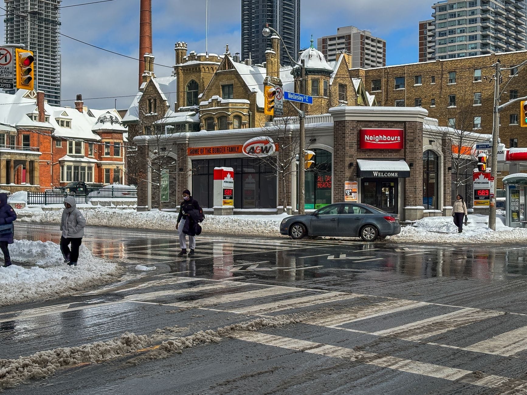 Cruzamento de ruas nevadas em Toronto com pedestres atravessando, carros e edifícios históricos e modernos de médio porte no inverno, mostrando por que o PATH pode ser útil.
