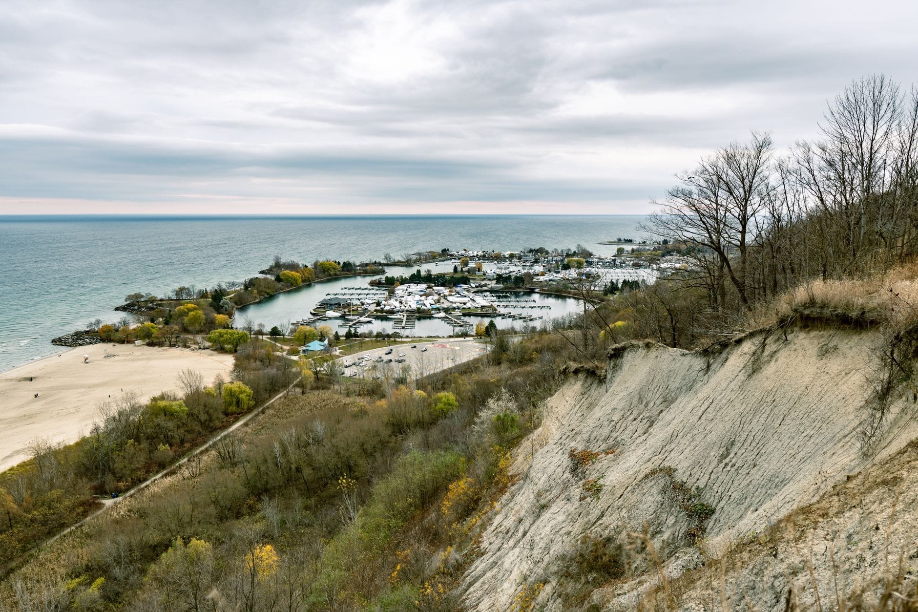 Vista dos Scarborough Bluffs de Toronto com penhascos acidentados, ravina arborizada, praia de areia e a margem do lago Ontario sob um céu nublado.