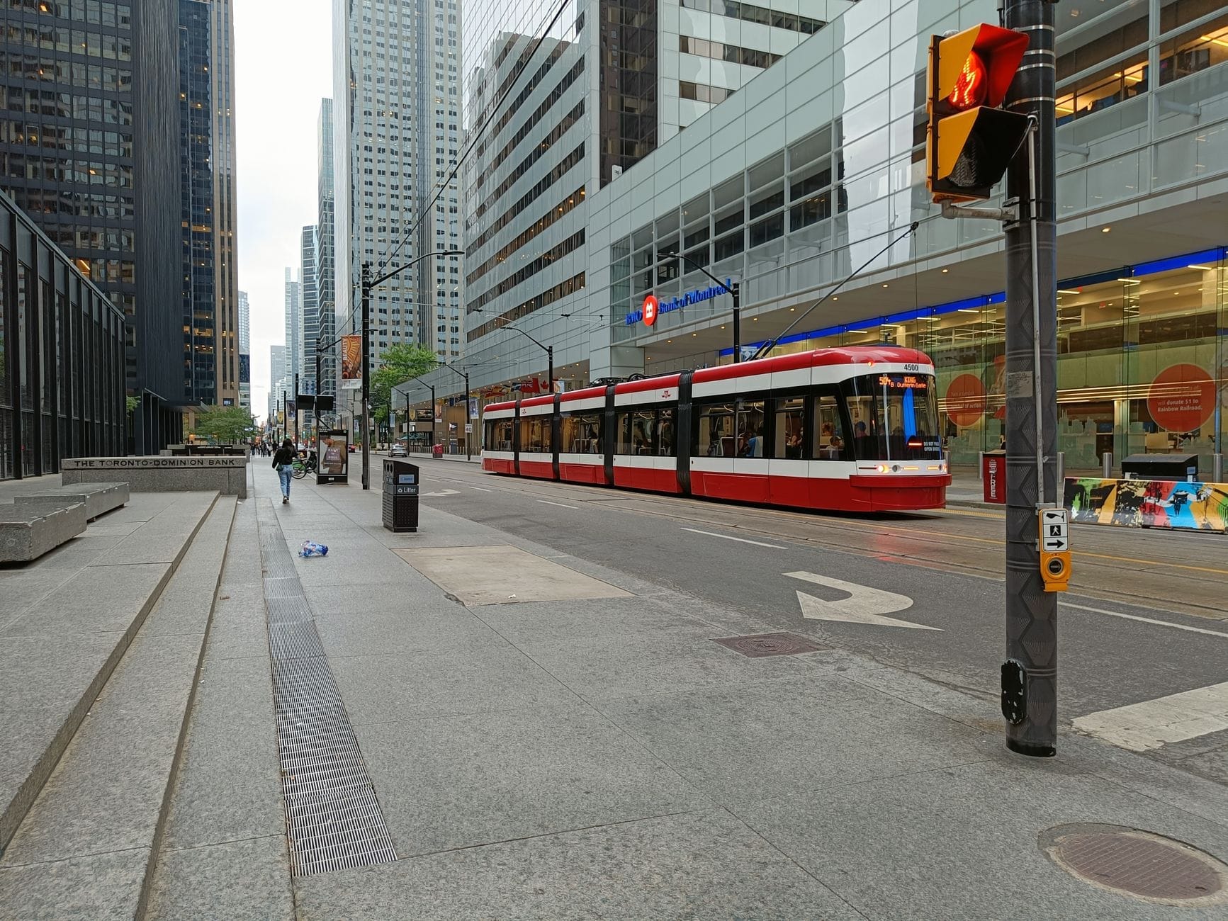 Bonde moderno vermelho e branco de Toronto percorrendo o centro da cidade com altos edifícios de vidro e cena urbana durante o dia.