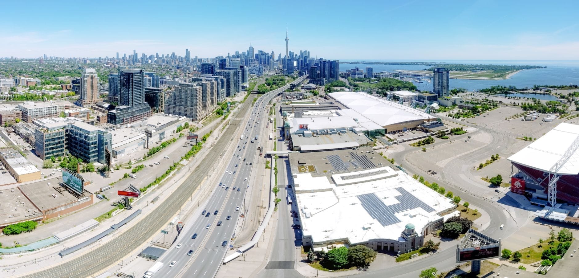 Vista aérea panorâmica da orla de Toronto mostrando o horizonte urbano, a CN Tower, as vias, os parques à beira do lago e as características da orla em um dia claro.