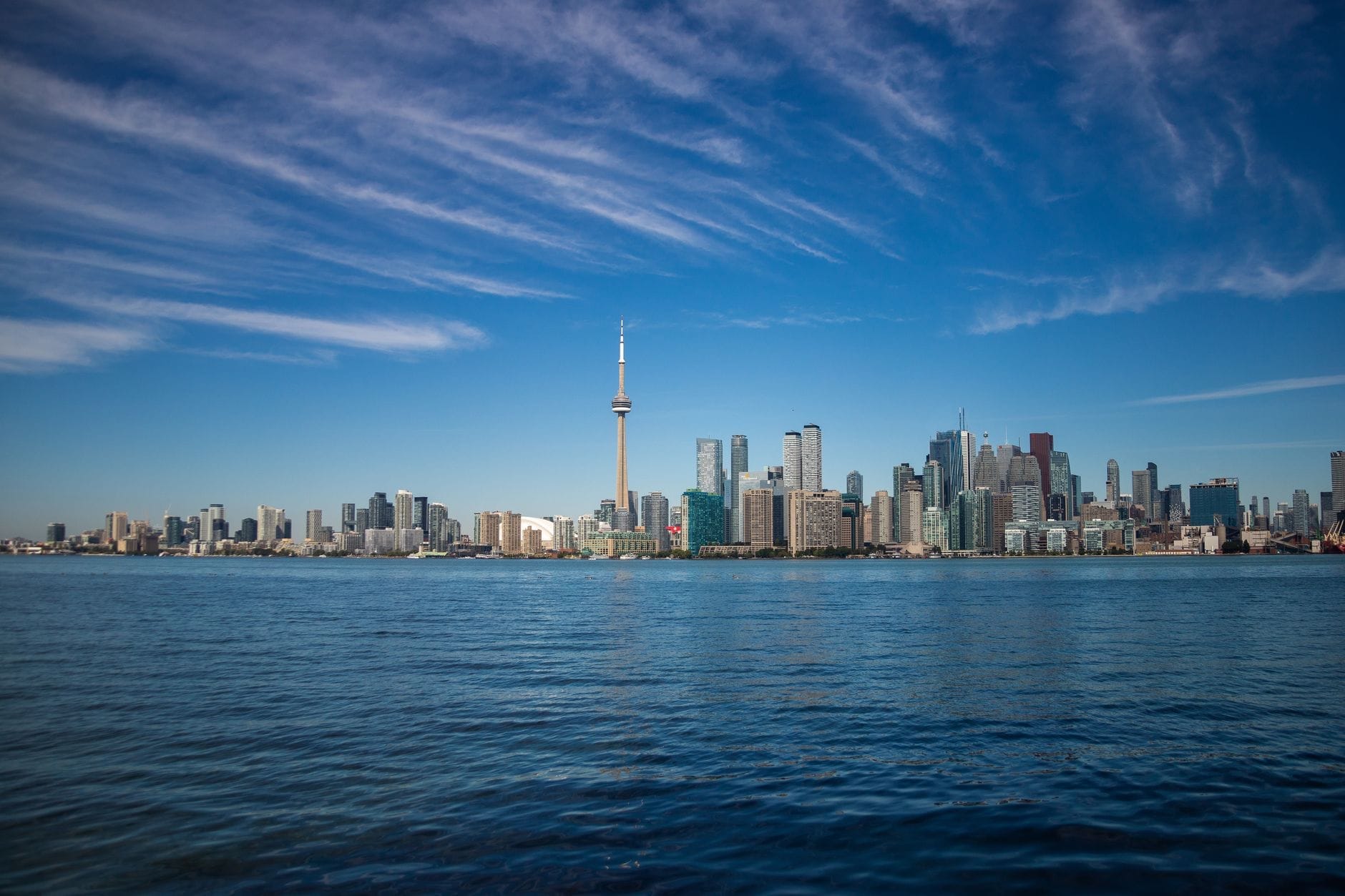 Vista panorâmica do skyline da orla de Toronto em um dia ensolarado, com céu azul e as águas calmas do lago em primeiro plano.