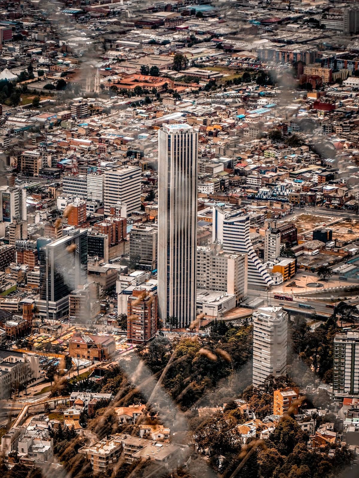 Aerial view of Bogotá cityscape featuring the tall Torre Colpatria surrounded by diverse buildings under partly cloudy skies.