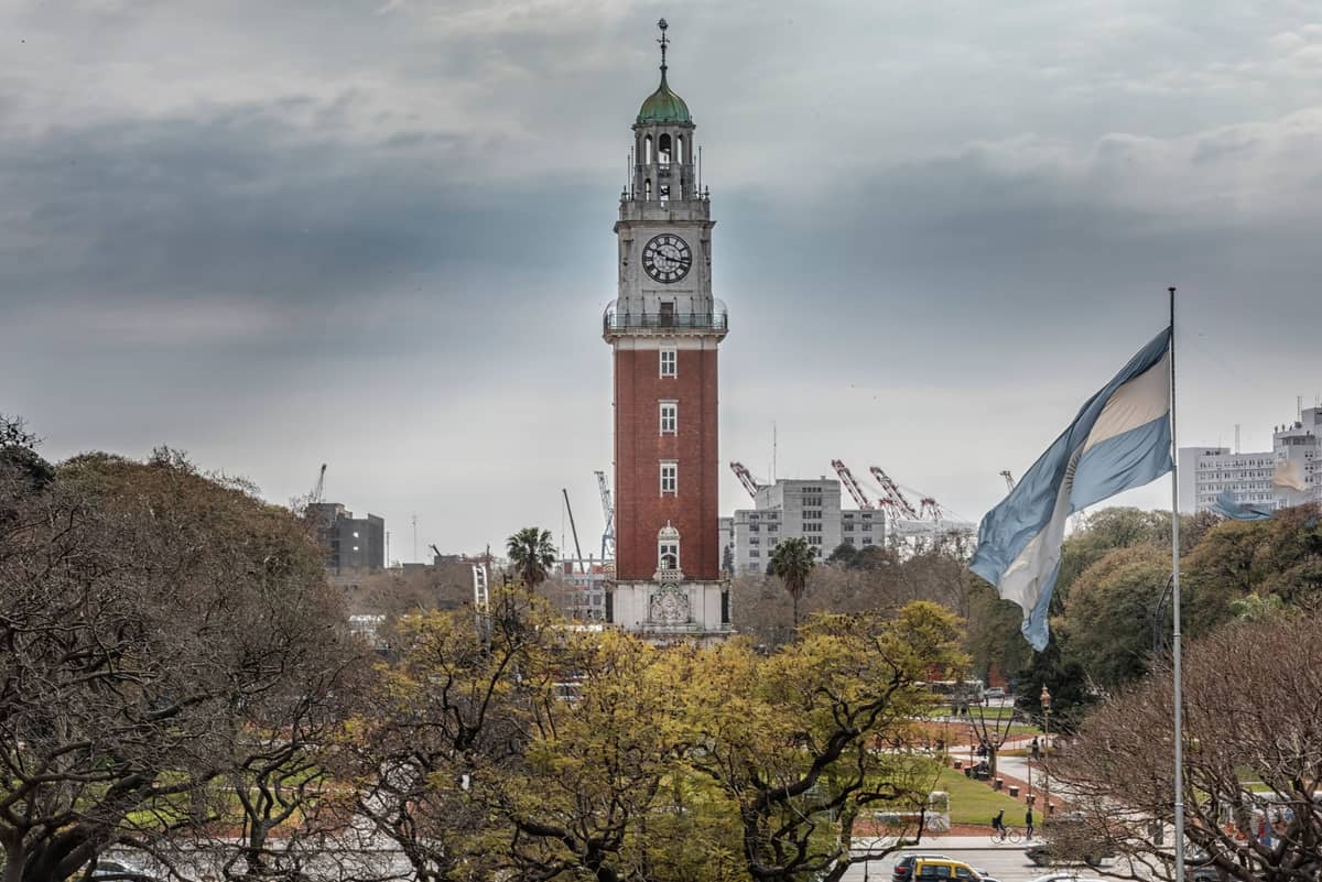 หอนาฬิกา Torre Monumental โดดเด่นเหนือยอดไม้กับธงชาติอาร์เจนตินาโบกด้านหน้า เบื้องหลังเห็นปั้นจั่นและทิวทัศน์เมืองบัวโนสไอเรส
