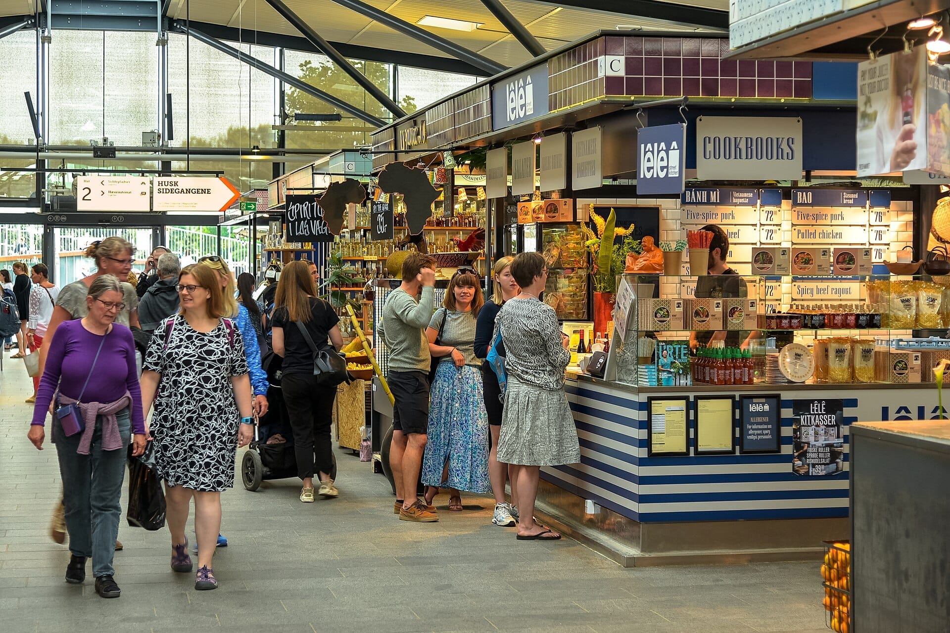 Gli acquirenti esplorano vari banchi gastronomici e venditori all'interno del vivace e luminoso mercato alimentare Torvehallerne a Copenaghen, Danimarca.