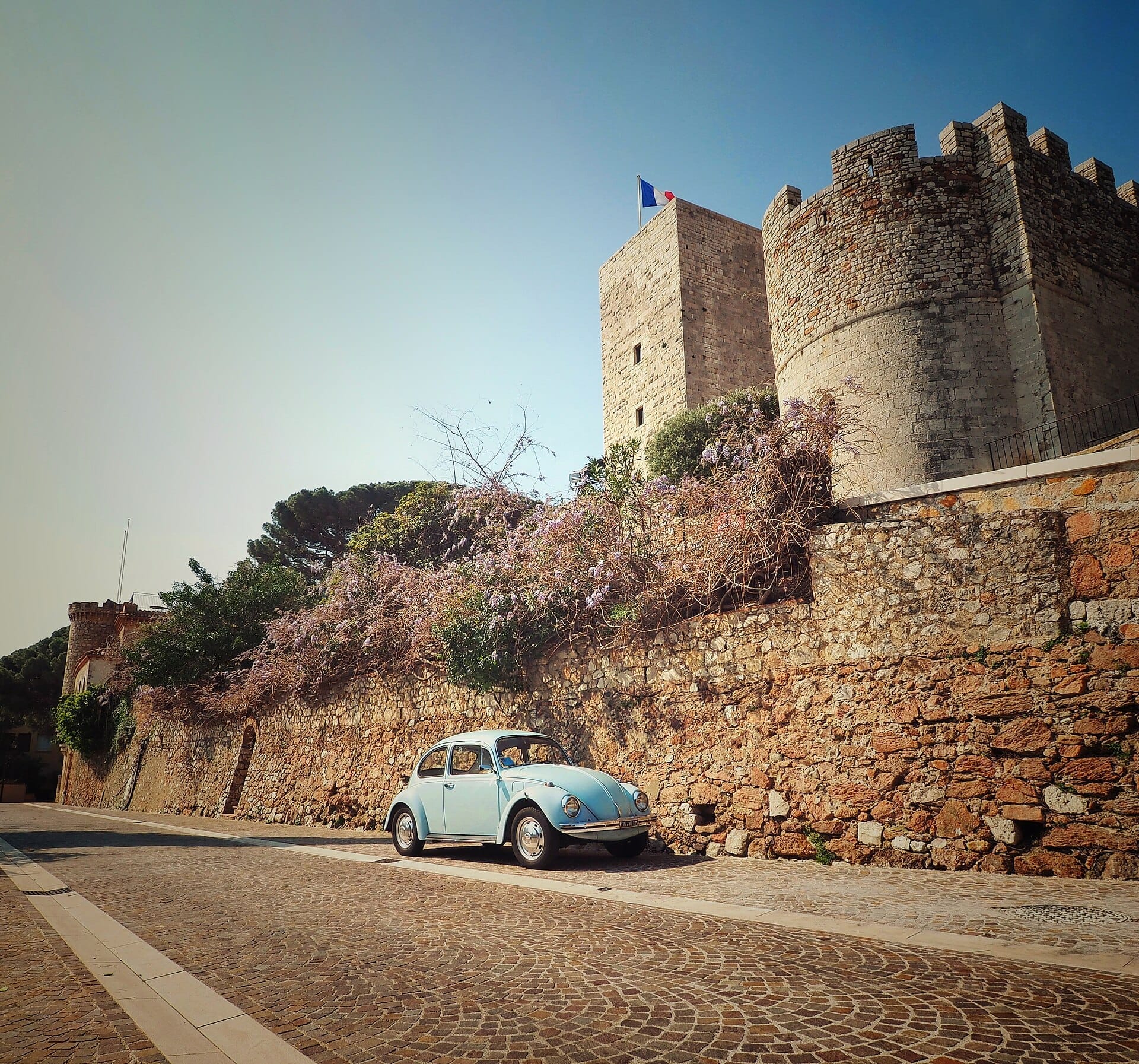 La torre di pietra del Tour du Suquet si erge sopra le antiche mura, con una classica auto blu parcheggiata su una soleggiata strada acciottolata a Cannes.
