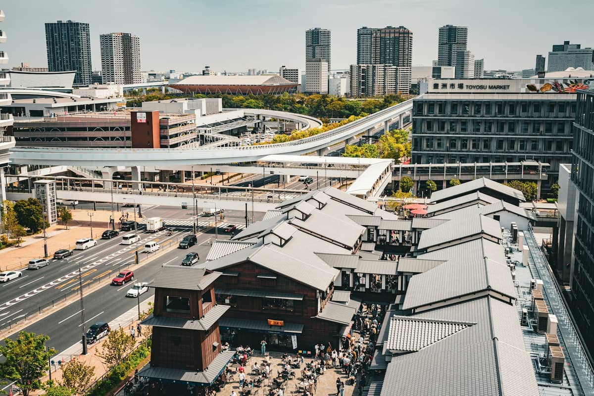 Aerial view of Toyosu Market buildings and outdoor plaza in Tokyo, surrounded by modern infrastructure and cityscape on a clear day.