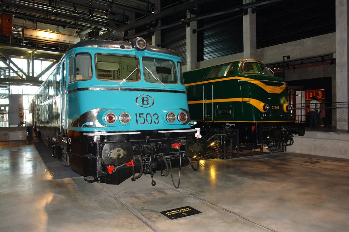 Duas locomotivas históricas em exposição no Train World de Bruxelas, o museu ferroviário nacional da Bélgica, com o interior moderno do museu e painéis de sinalização ao fundo.