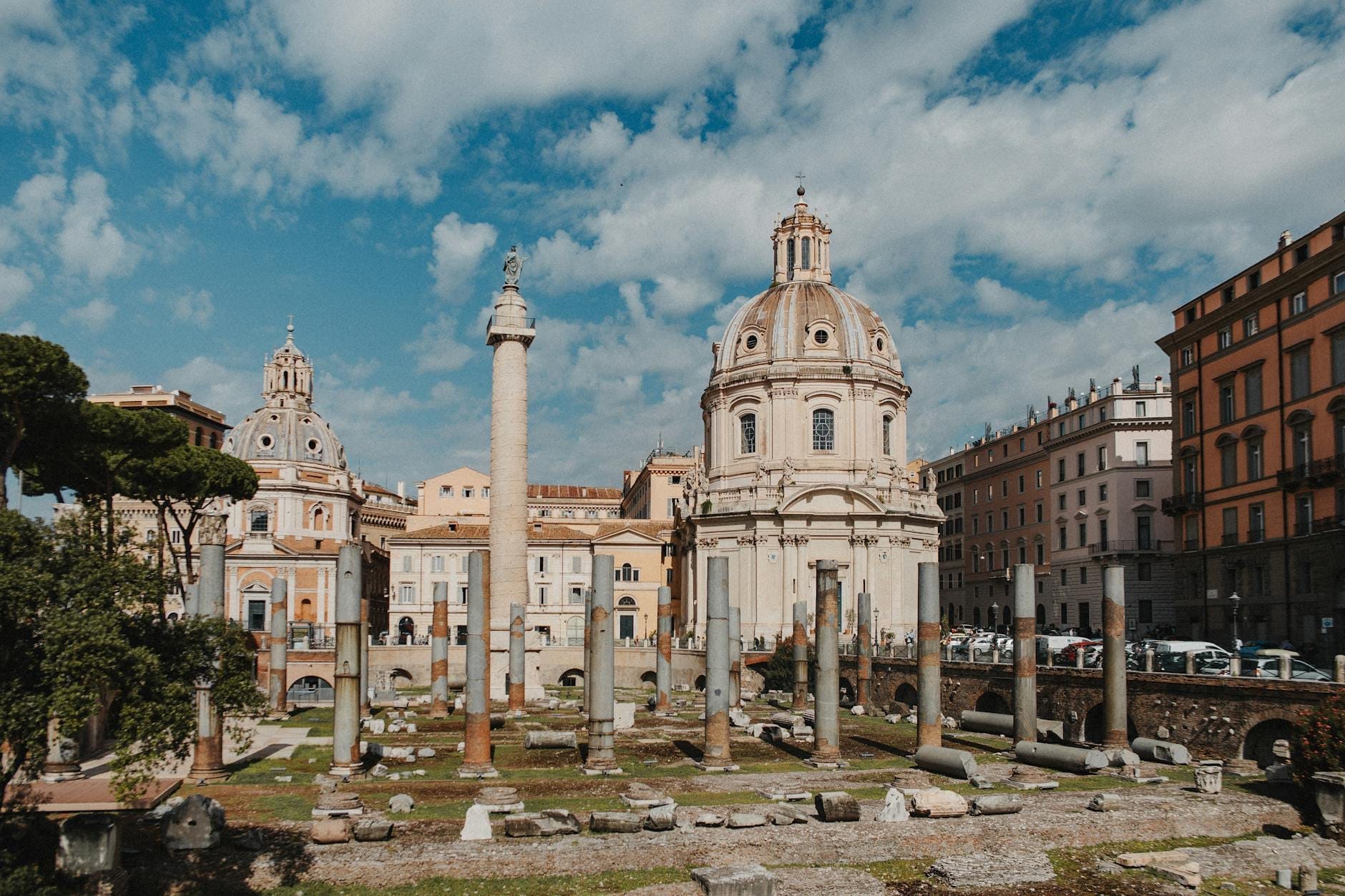 Trajan's Column standing prominently among ancient ruins with domed churches and blue sky in the historical center of Rome, Italy.