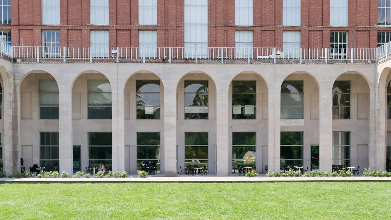 Facciata del Triennale Milano Design Museum con grandi archi, ampie finestre e un prato verde davanti alla luce del giorno.