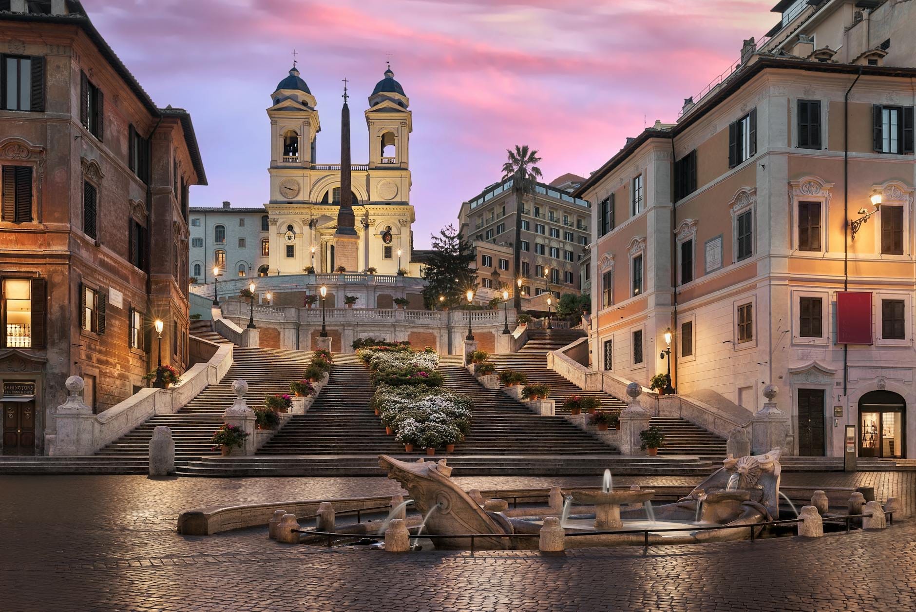 Trinità dei Monti church with its twin towers above the Spanish Steps, early morning with empty steps and surrounding piazza, under a pink and purple sky.