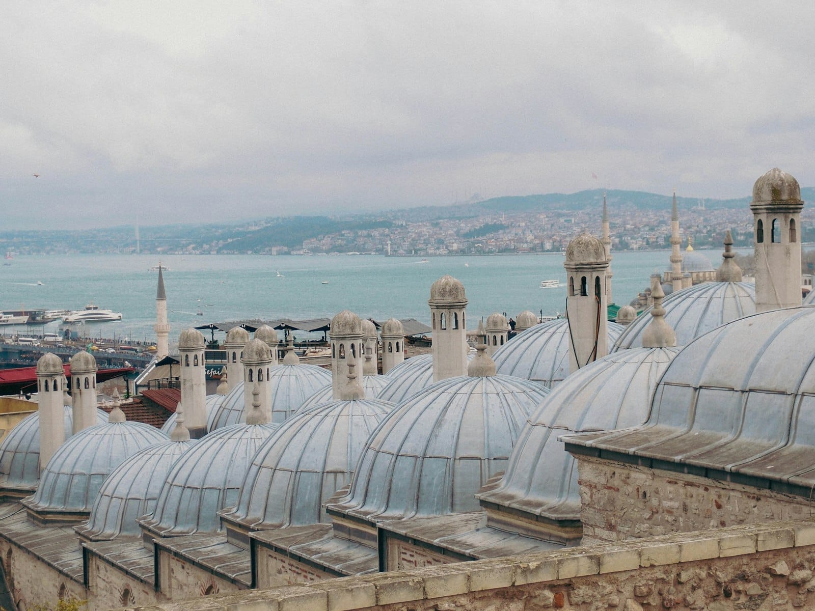 Cúpulas de um histórico hamam de Istambul com o Bósforo ao fundo sob um céu nublado.