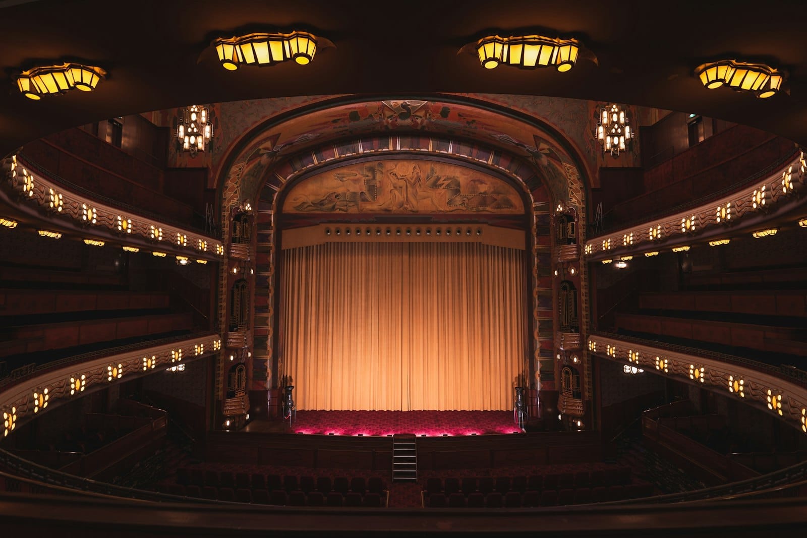 Vista interior elegante del Pathé Tuschinski Theater en Ámsterdam, con luces art déco, balcones ornamentados y un telón de escenario dorado.