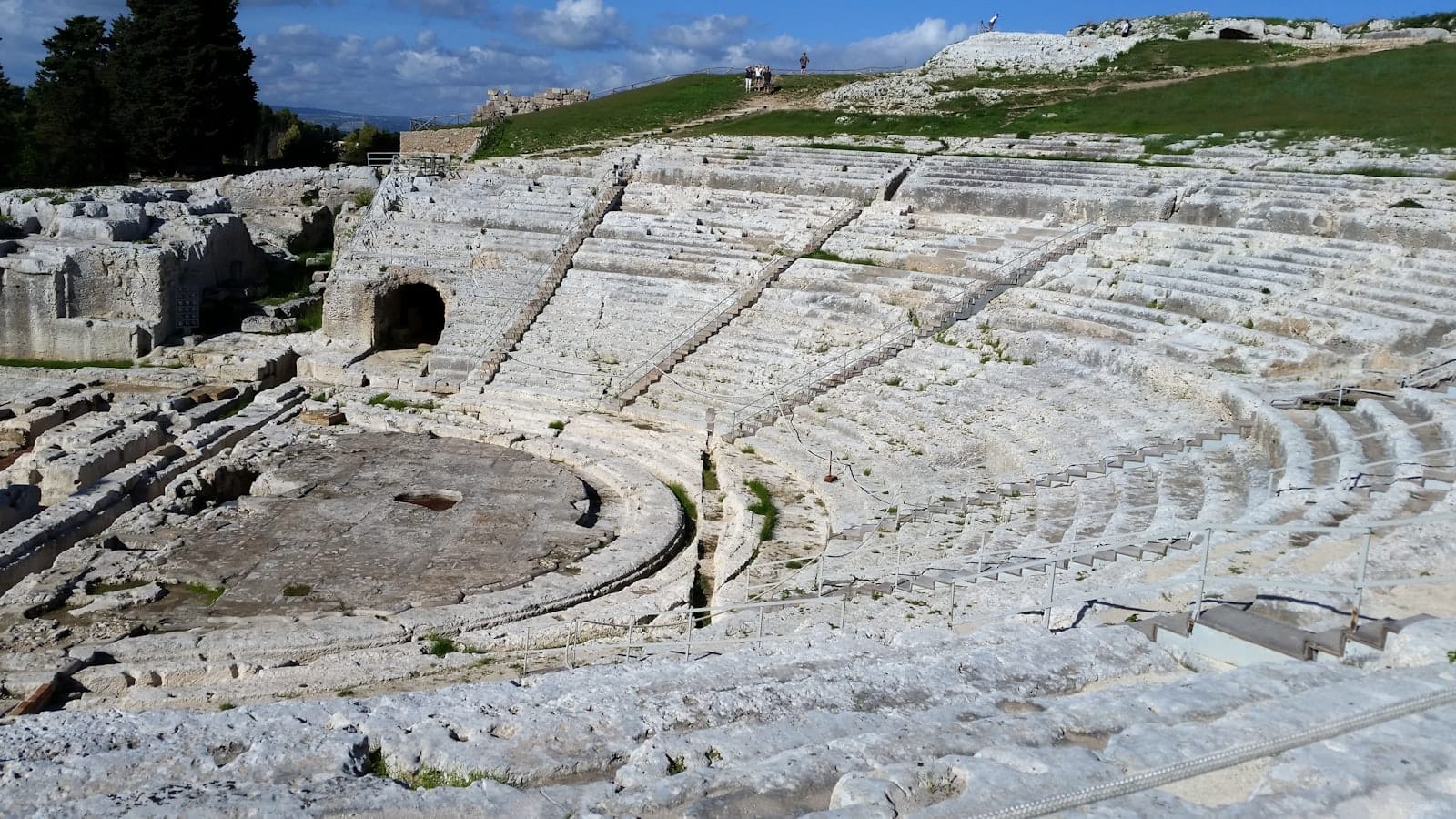 Weitblick auf das antike griechische Theater in Syrakus, Sizilien, mit Steinsitzen und grünem Gras darüber.