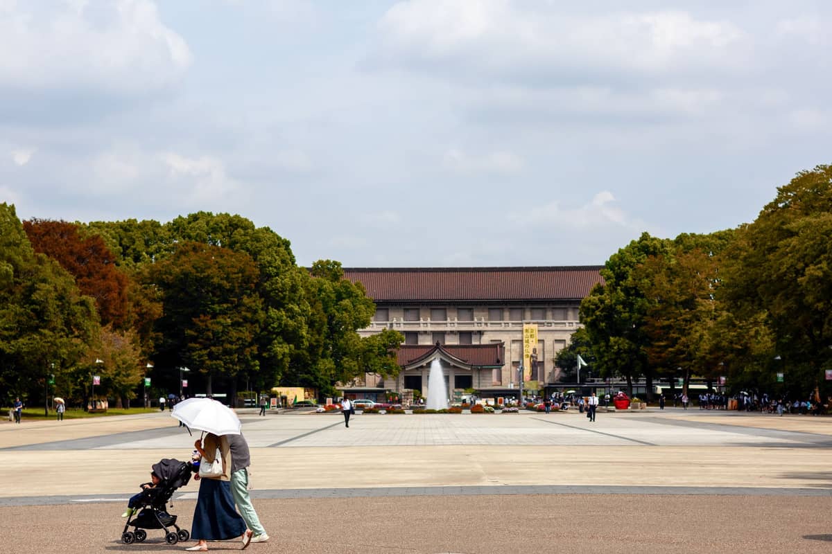 Wide central plaza of Ueno Park with people walking and the Tokyo National Museum building visible in the background under a partly cloudy sky.