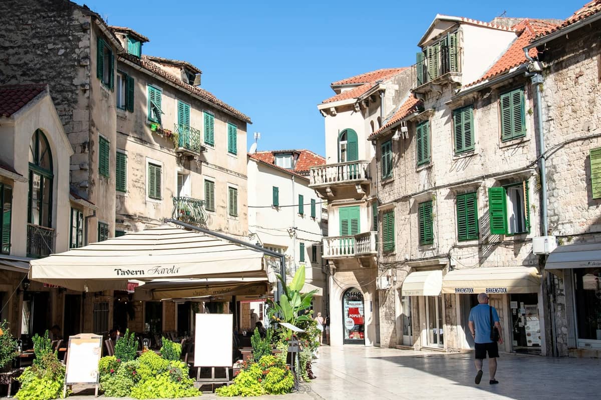 Charming square in Split with historic stone buildings, green window shutters, cafes, and a pedestrian, evoking the city’s vibrant accommodation scene.