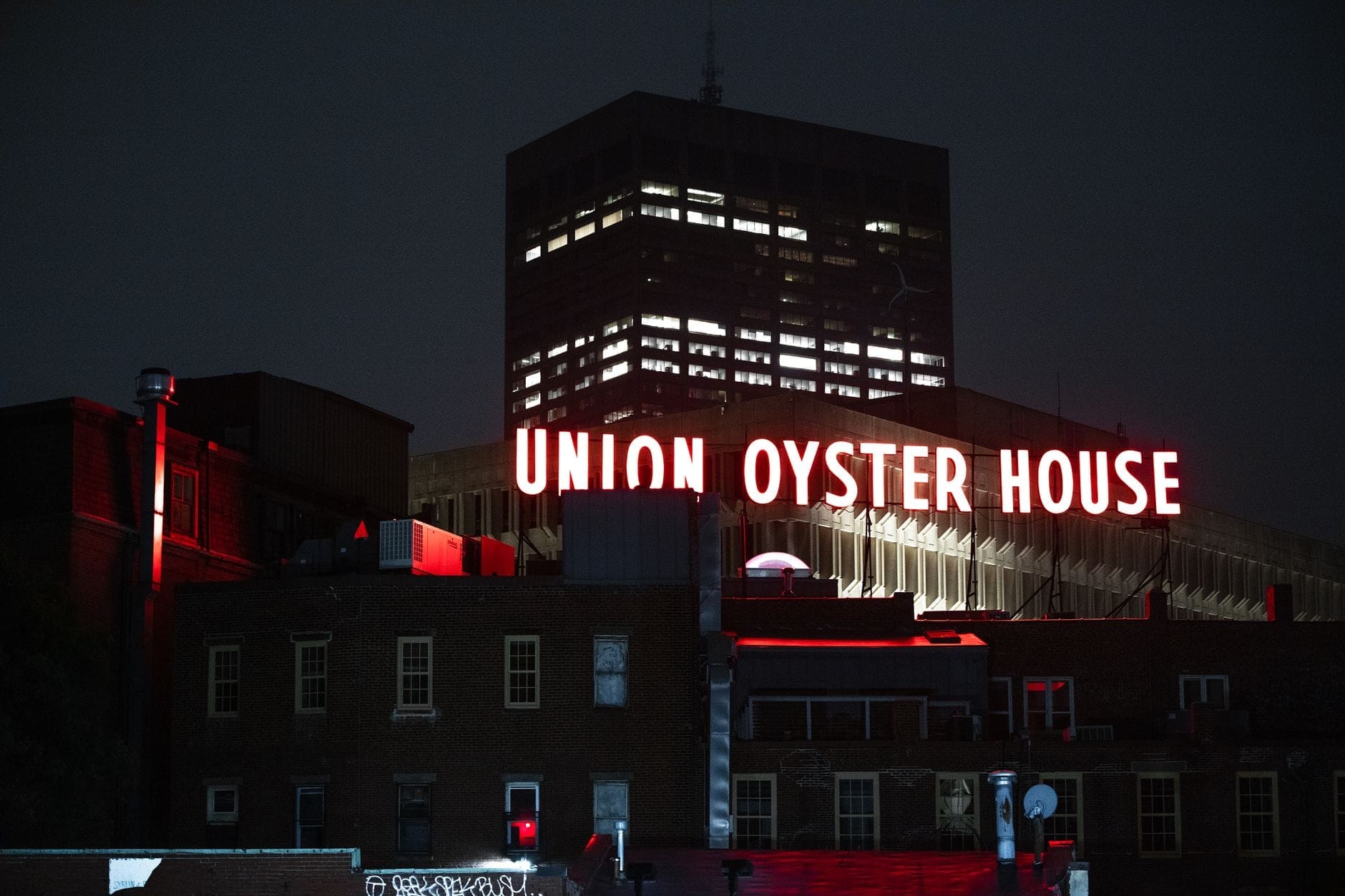 Vista notturna dell'insegna al neon dell'Union Oyster House che brilla sopra gli storici edifici in mattoni di Boston, con un moderno grattacielo sullo sfondo.