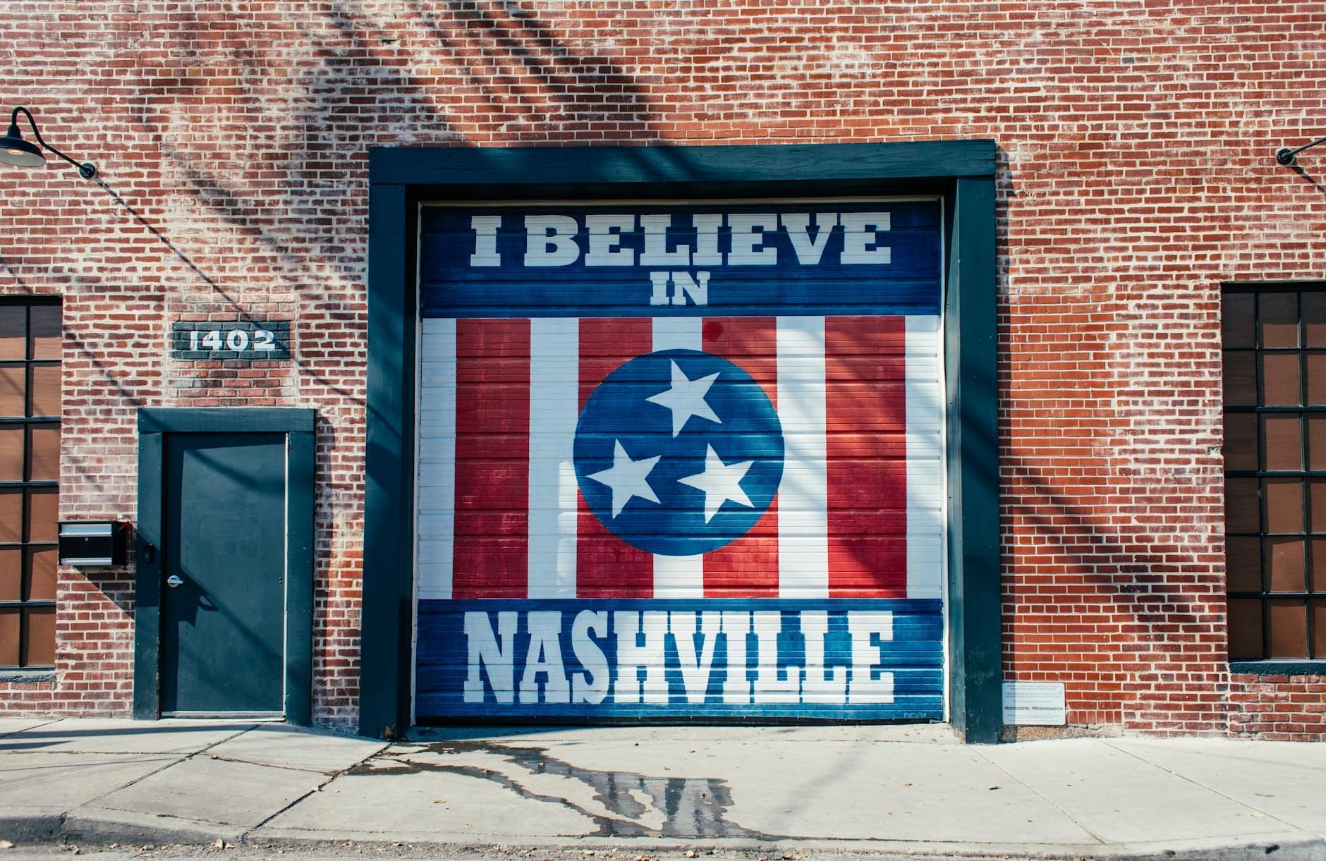 Un conocido mural 'I Believe in Nashville' pintado en una puerta de garaje en un edificio de ladrillo rojo con un entorno urbano.