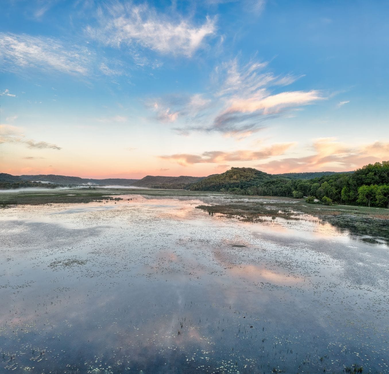 Un amplio río o humedal con agua reflectante, rodeado de colinas boscosas al atardecer cerca de Nashville.