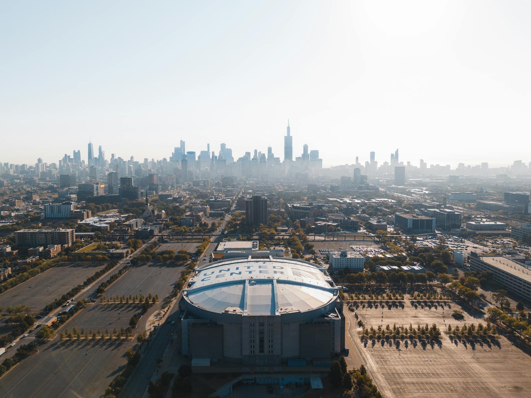 Vista aerea dello United Center con lo skyline di Chicago sullo sfondo, che mostra il palazzetto e i suoi ampi parcheggi in una giornata limpida.