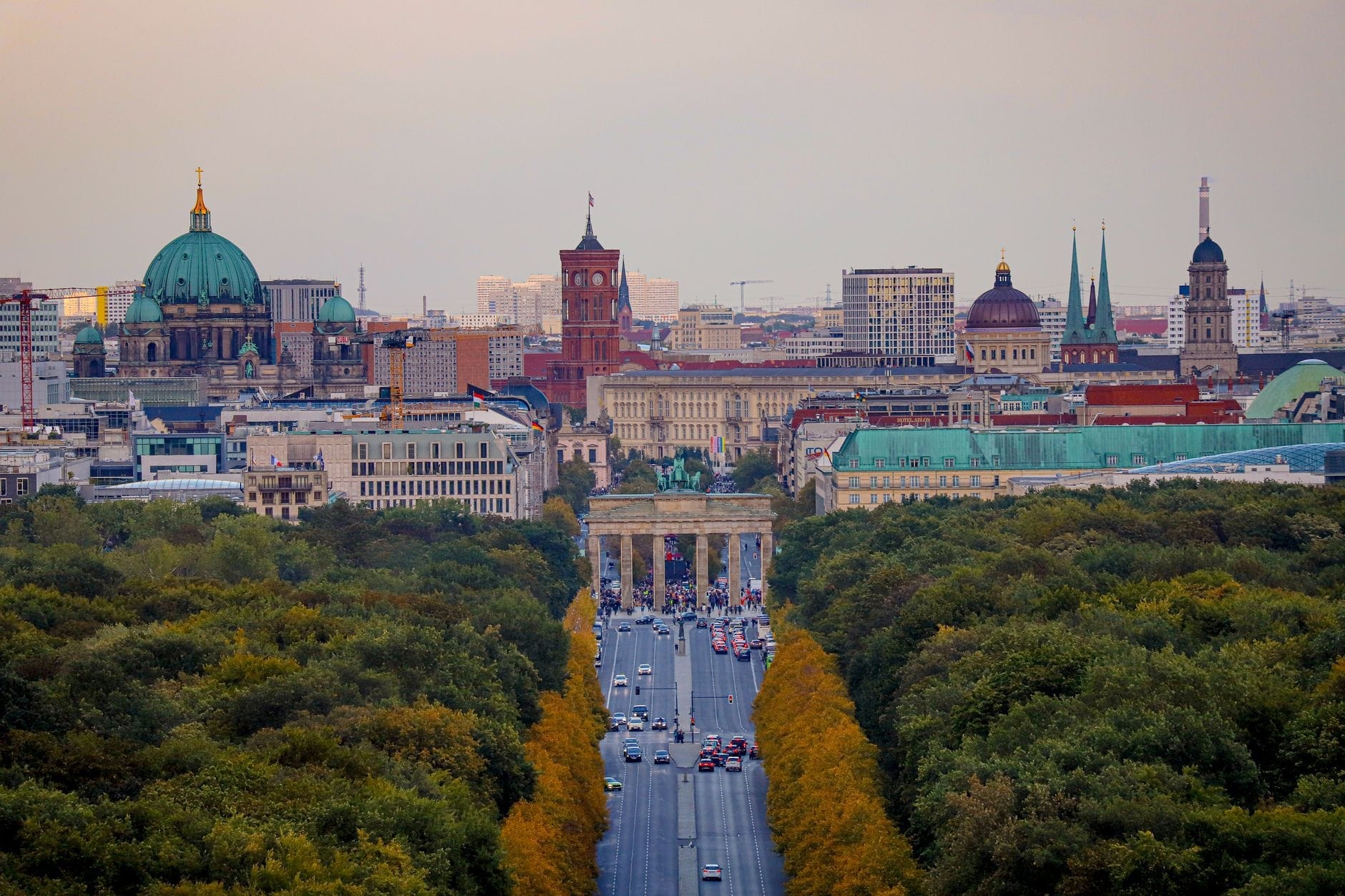Vista aerea del viale Unter den Linden a Berlino, fiancheggiato da alberi verdi, con la Porta di Brandeburgo sullo sfondo e i monumenti storici della città.