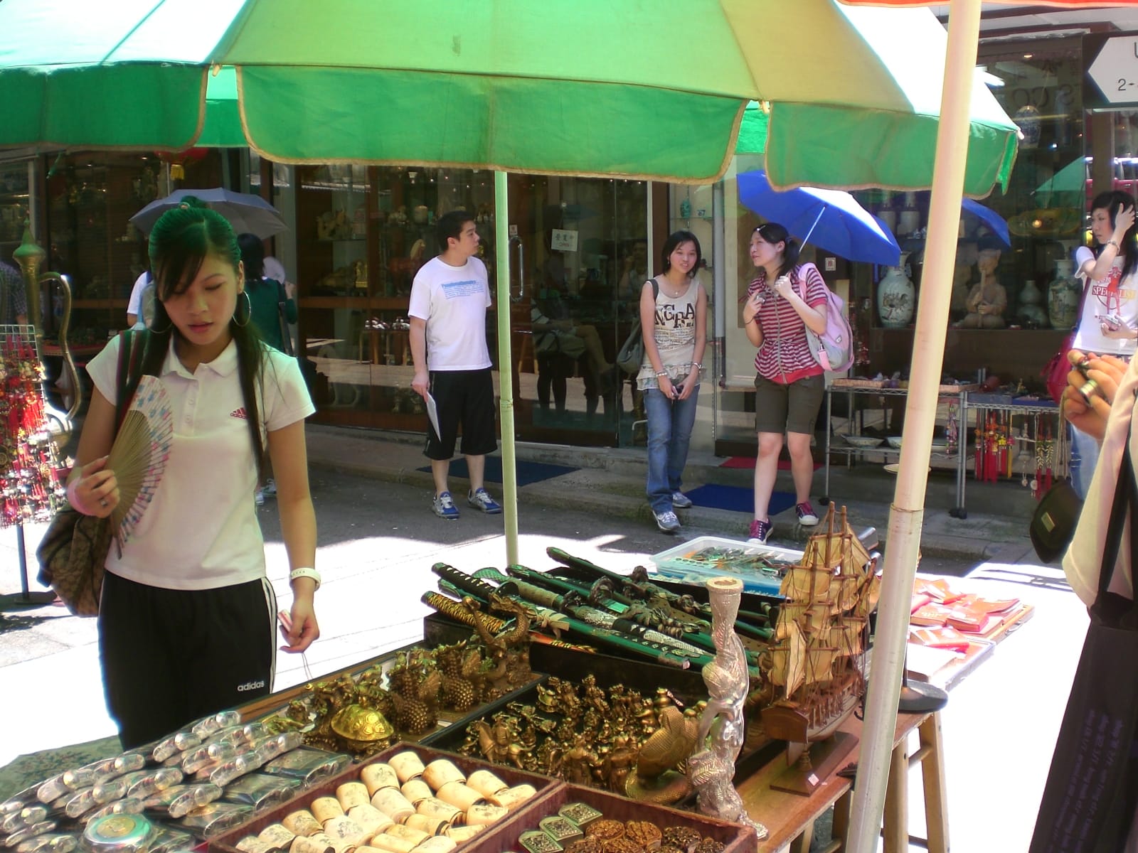 Negozi e bancarelle animate lungo Upper Lascar Row (Cat Street) a Hong Kong, con antiquariato e curiosità esposti su scaffali colorati del mercato.