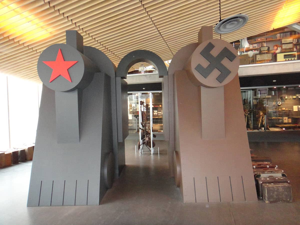 Ausstellungsraum im Vabamu Museum mit symbolischen Torbögen, die sowjetische und nationalsozialistische Embleme tragen, im Hintergrund Vitrinen mit Exponaten.