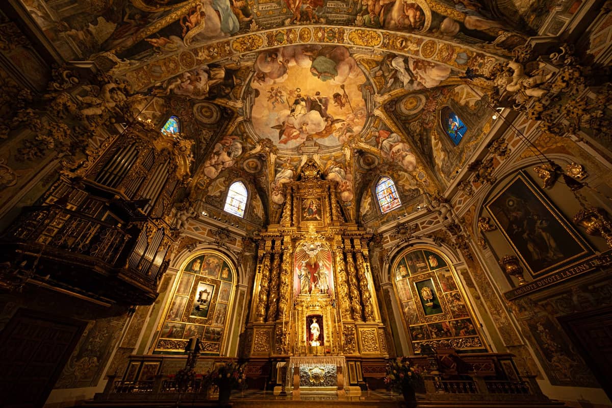 Interno di chiesa barocca sontuosamente decorato a Valencia con altare dorato, affreschi ornati e dettagliate opere d'arte sul soffitto.
