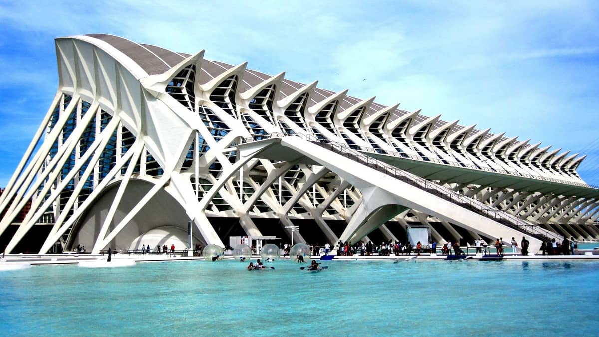 Il Museu de les Ciències Príncipe Felipe con persone che si godono la piscina bassa e il sole, architettura moderna bianca e un cielo estivo azzurro intenso a Valencia.