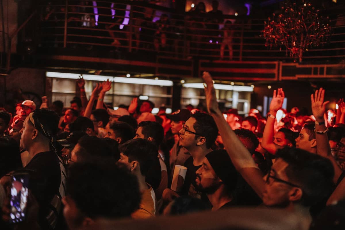 Grande folla che si diverte in una vivace notte in una discoteca di Valencia, con le mani alzate e luci rosse colorate sotto un elegante balcone.