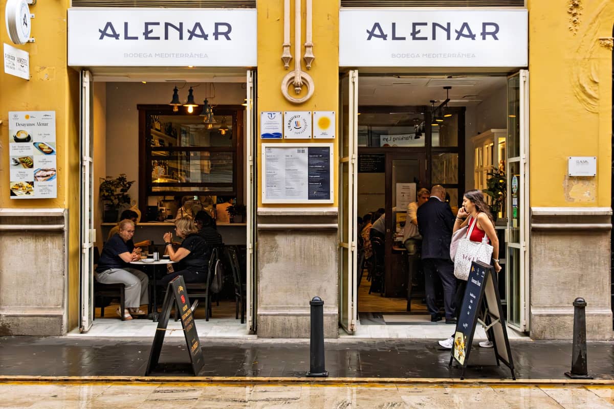 Menschen beim Abendessen und geselligen Beisammensein in einer gut beleuchteten Bar oder Bodega mit offenen Türen in einer Straße in Valencia