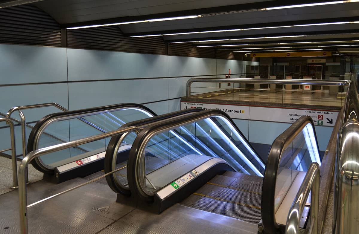 Scale mobili che scendono verso le linee 3 e 5 della Metro Valencia alla stazione Aeropuerto, con segnali chiari per il collegamento metro-aeroporto.