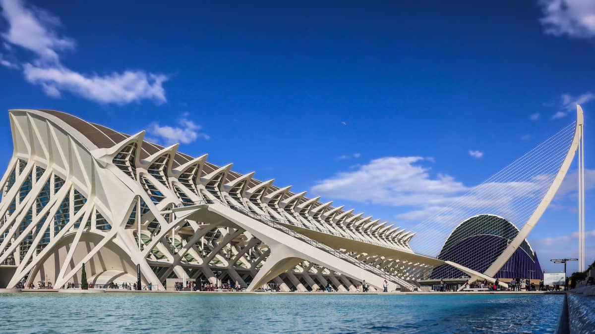 Le strutture bianche e futuristiche della Città delle Arti e delle Scienze di Valencia, che si specchiano in una piscina riflettente azzurra in una luminosa giornata di sole.