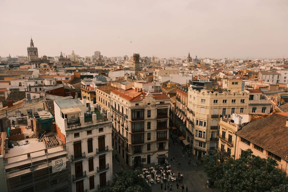 Una amplia vista sobre el centro de la ciudad de Valencia con edificios históricos, calles animadas y personas reunidas en cafés al aire libre.