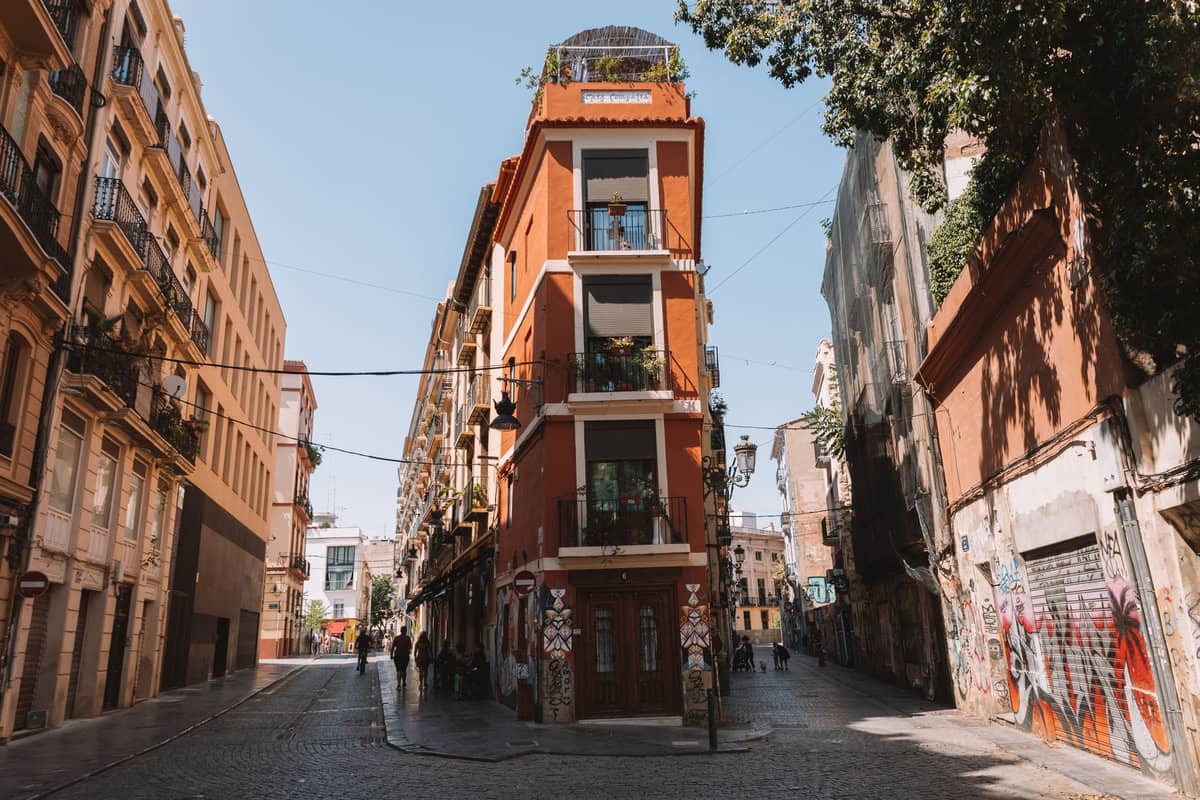 Una amplia calle peatonal en Valencia con edificios históricos, grafitis y personas caminando durante el día.
