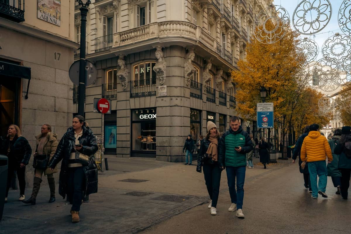 Ludzie spacerują szeroką ulicą dla pieszych, wzdłuż której stoją eleganckie zabytkowe budynki i sklepy w Valencii.