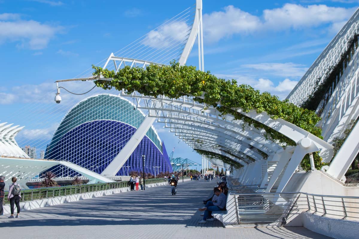 Walkway at the City of Arts and Sciences in Valencia, Spain, with the L'Hemisfèric building and modern white structures in the background under a blue sky.