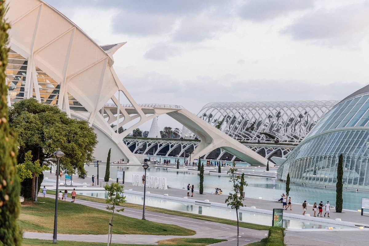 Vista panoramica della Città delle Arti e delle Scienze di Valencia, con edifici bianchi futuristici, cupole di vetro, specchi d'acqua e visitatori che passeggiano intorno alle vasche.